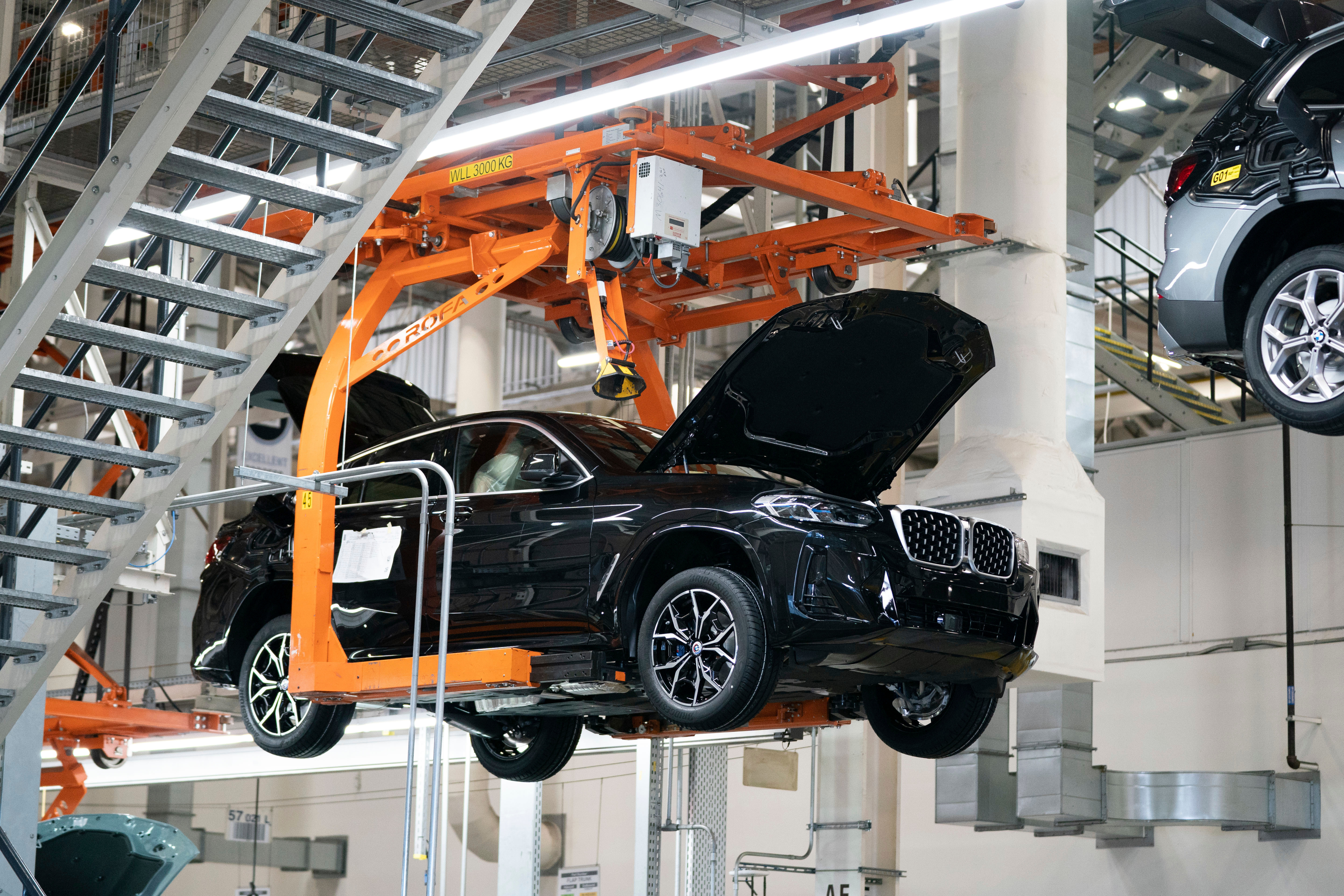 Black SUV suspended by orange mechanical lift in automotive manufacturing facility