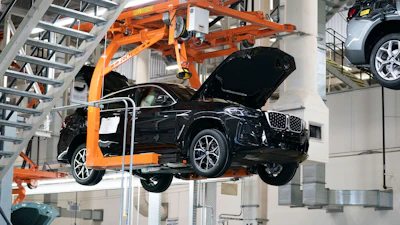 Black SUV suspended by orange mechanical lift in automotive manufacturing facility