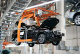 Black SUV suspended by orange mechanical lift in automotive manufacturing facility
