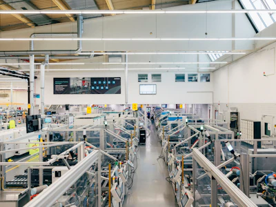 Modern industrial manufacturing facility with machinery, workstations, and safety railings in a bright warehouse setting