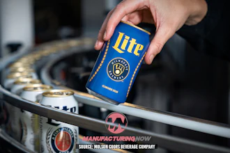 Hand holding blue Miller Lite beer can above industrial manufacturing equipment