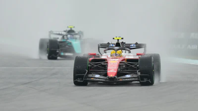 Formula 1 racing cars competing on a wet track in rainy conditions, with red and black vehicles leading the field.