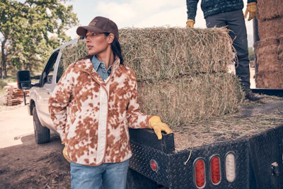 Woman in brown and white jacket standing by hay bale on farm truck