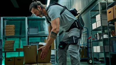 Worker in gray shirt and tool belt organizing cardboard boxes in a modern warehouse with teal shelving.