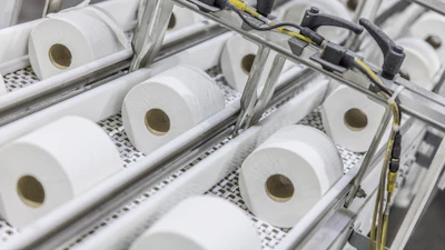 Industrial production line with multiple white tissue paper rolls on conveyor system with mechanical components and yellow wiring