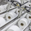 Industrial production line with multiple white tissue paper rolls on conveyor system with mechanical components and yellow wiring