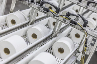Industrial production line with multiple white tissue paper rolls on conveyor system with mechanical components and yellow wiring