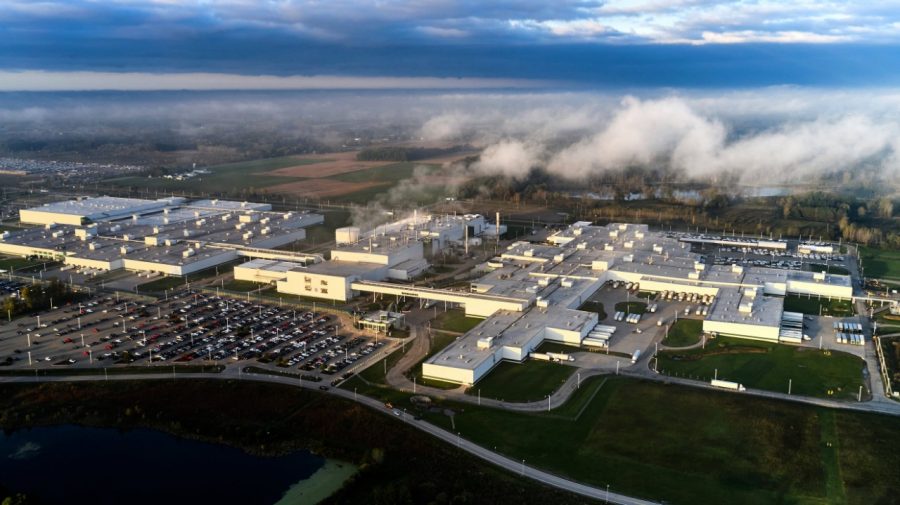 Aerial view of large industrial manufacturing complex with warehouse facilities, parking areas, and surrounding countryside landscape under cloudy sky