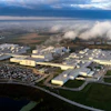 Aerial view of large industrial manufacturing complex with warehouse facilities, parking areas, and surrounding countryside landscape under cloudy sky