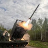 Military MLRS launcher firing a long-range missile in a forest clearing with smoke and flames visible