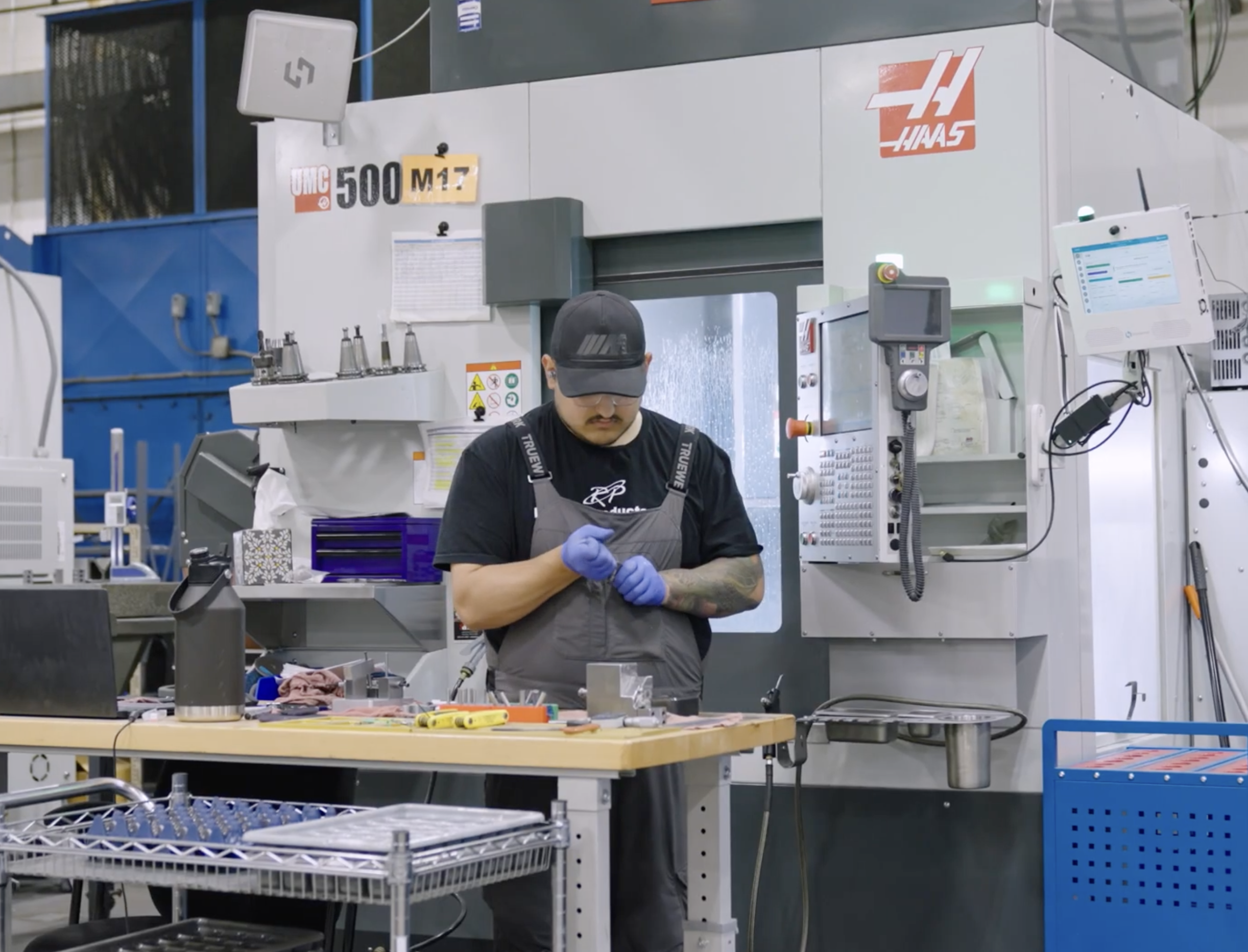 Machinist in blue gloves working at a HAAS CNC machine in an industrial manufacturing facility.