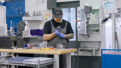 Machinist in blue gloves working at a HAAS CNC machine in an industrial manufacturing facility.