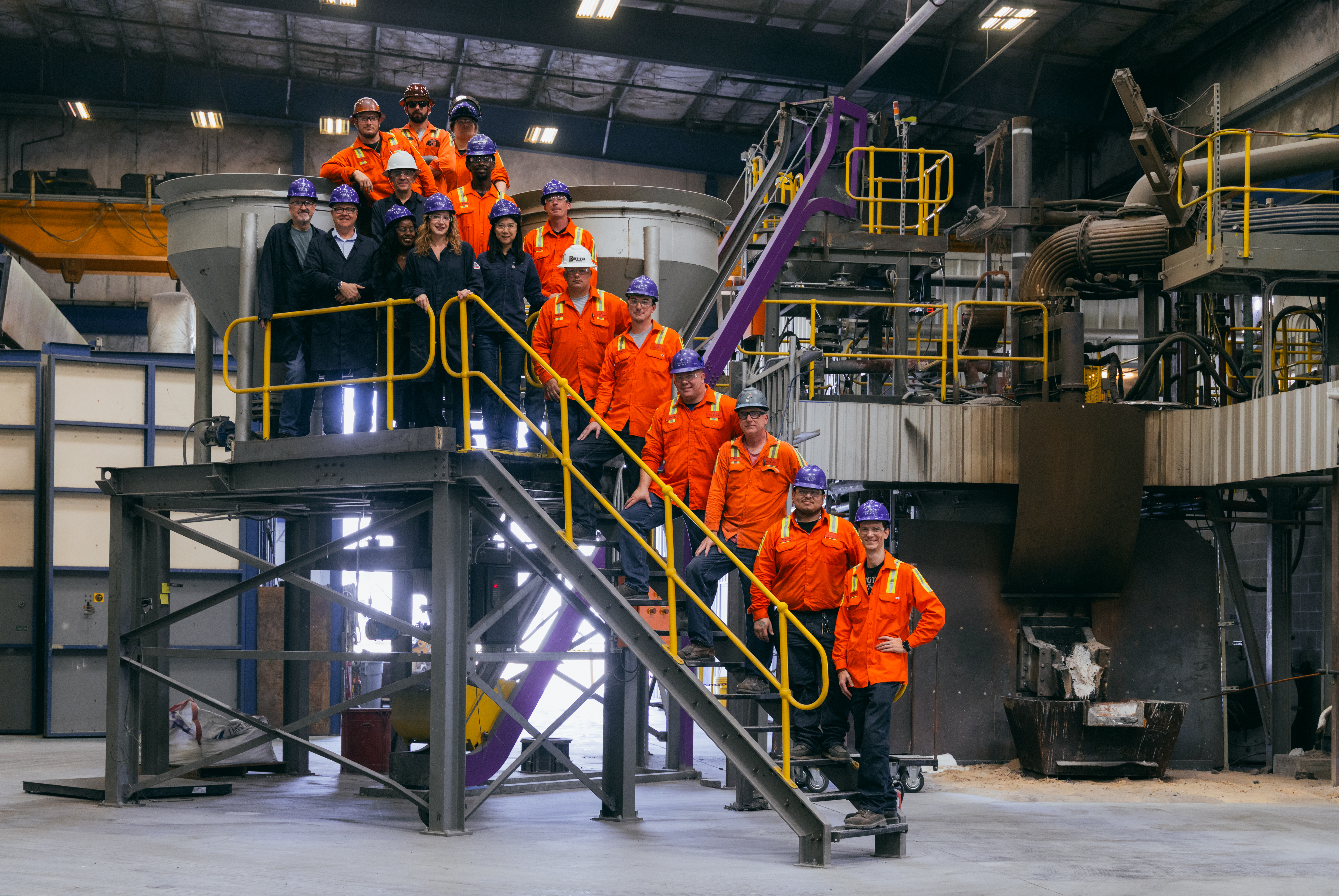 Industrial facility tour with group in orange safety uniforms on yellow metal stairs and platforms