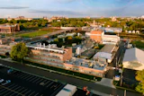 Aerial view of brick industrial complex with parking lot, green spaces, and surrounding cityscape