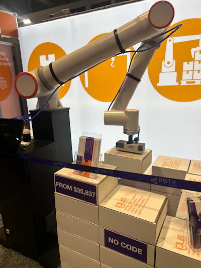 Gold robotic arm on display stand at trade show with RBTX branding and pricing signage
