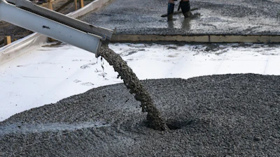 Concrete being poured from a chute during construction work on a wet surface