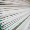 Close-up view of stacked drywall sheets showing white and teal-tinted edges layered together