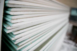 Close-up view of stacked drywall sheets showing white and teal-tinted edges layered together