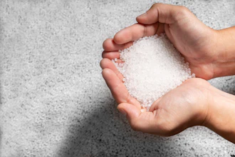 Hands holding white salt or sugar crystals against concrete background