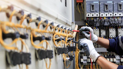 Electrician installing yellow wiring in industrial circuit breaker panel with safety gloves