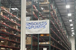 Industrial warehouse interior with tall storage racks, branded signage including Goulds Pumps and Rexnord logos, pallets, and orange safety markers on concrete floor.