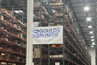 Industrial warehouse interior with tall storage racks, branded signage including Goulds Pumps and Rexnord logos, pallets, and orange safety markers on concrete floor.