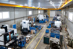 Industrial manufacturing facility with CNC machines, blue workbenches, and overhead yellow crane system in warehouse space