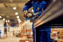 Industrial worker in blue uniform using angle grinder on metal with sparks flying in factory setting