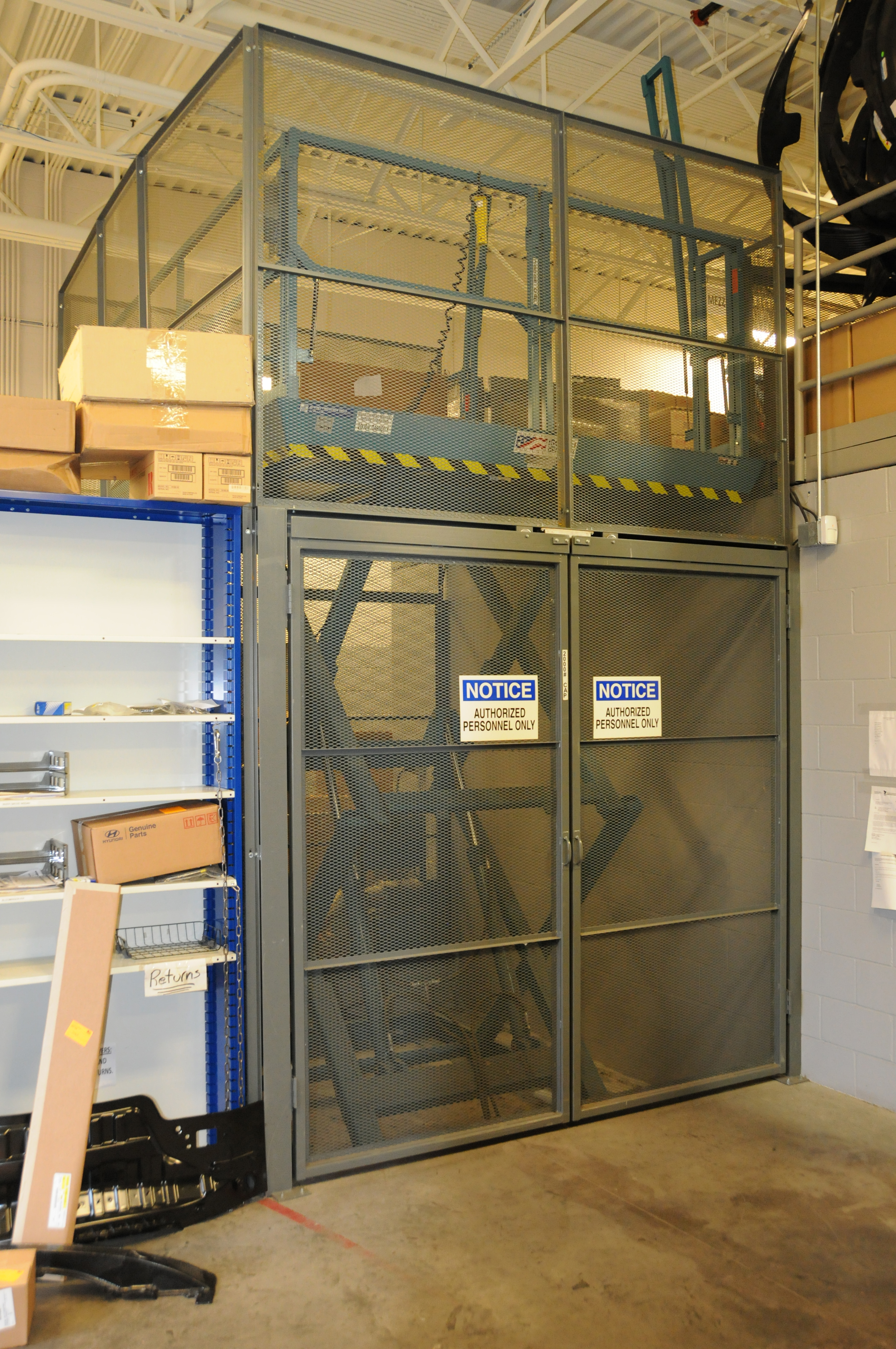 Industrial safety cage with mesh panels and yellow-black striping in warehouse facility