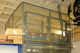 Industrial safety cage with mesh panels and yellow-black striping in warehouse facility