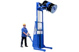 Worker operating blue industrial drum lifter with safety equipment for material handling