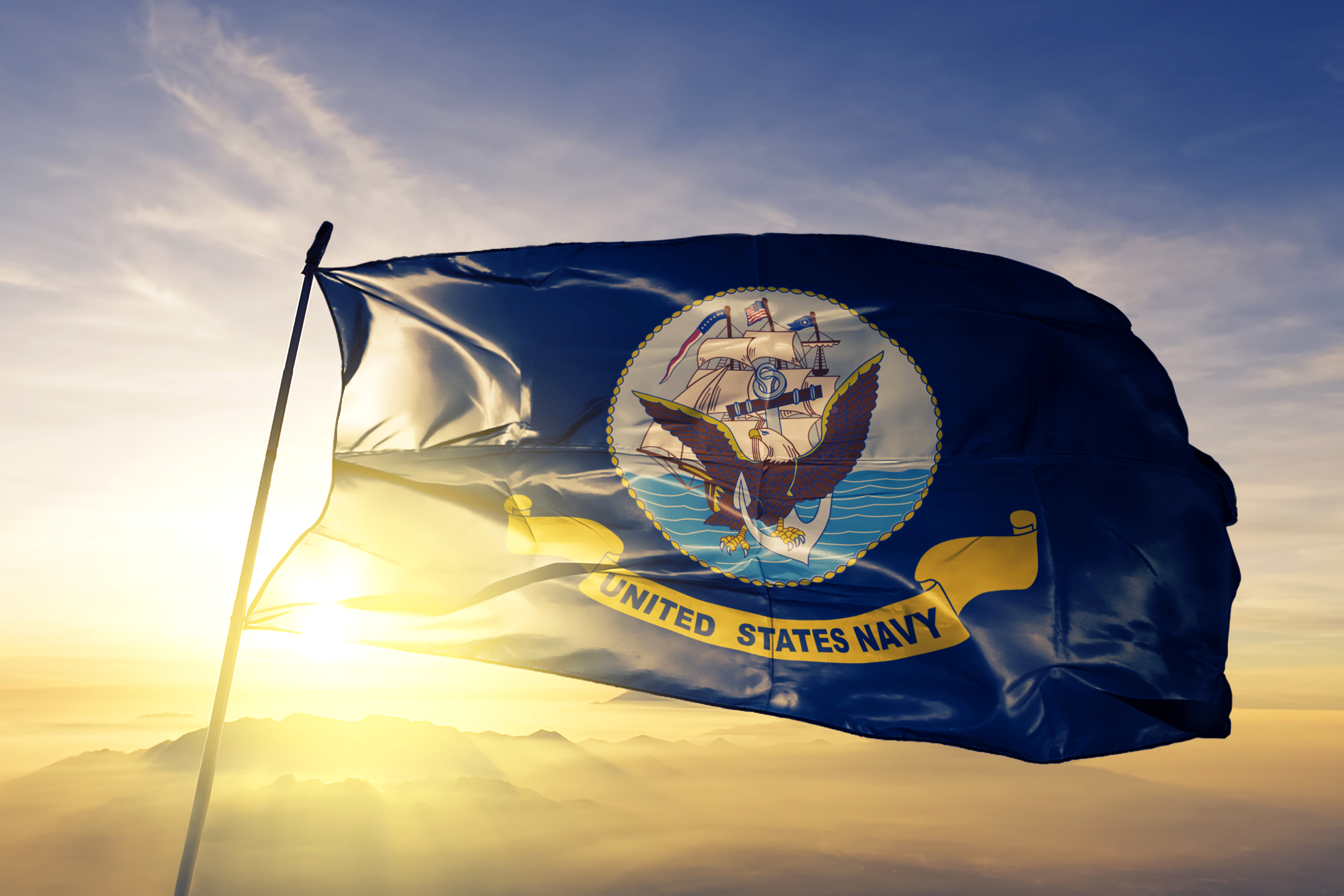 United States Navy flag waving against golden sunset sky with mountains in background