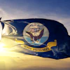 United States Navy flag waving against golden sunset sky with mountains in background