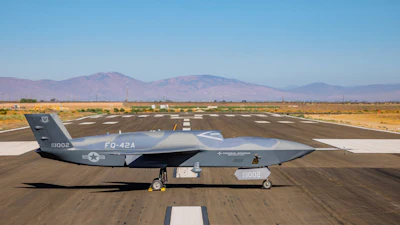 Gray RQ-4 Global Hawk military drone aircraft parked on desert runway with mountains in background