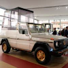Vintage Mercedes-Benz G-Class with white body and gold wheels displayed in modern showroom with visitors
