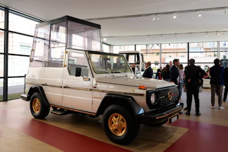 Vintage Mercedes-Benz G-Class with white body and gold wheels displayed in modern showroom with visitors