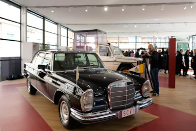 Classic black Mercedes-Benz sedan displayed in museum exhibition hall with visitors and vintage vehicles