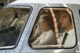 Two people seated in vintage aircraft cabin with sunlight streaming through windows