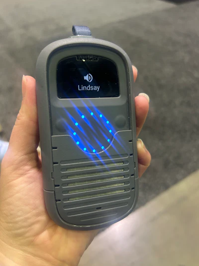 Person holding vintage mobile device with blue LED display showing 'Lindsay' caller name