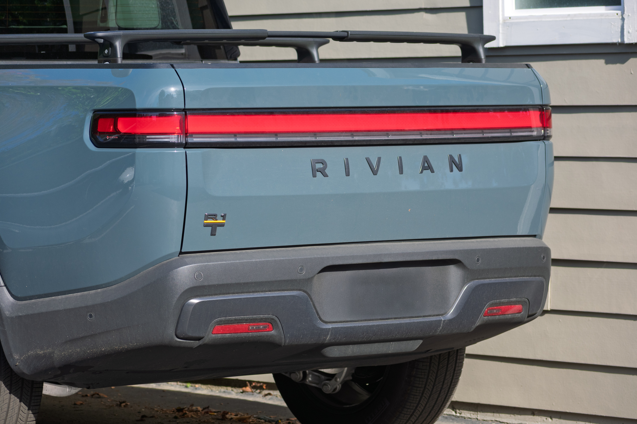 Rear view of light blue Rivian R1T electric truck with red horizontal tail lights and gray bumper
