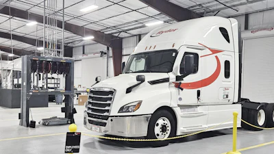 White Schneider semi-truck with red stripe parked in industrial warehouse facility with yellow safety barriers