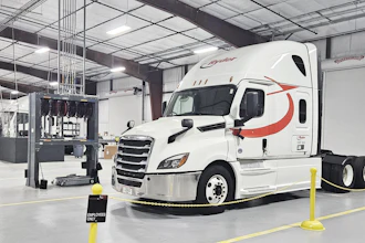 White Schneider semi-truck with red stripe parked in industrial warehouse facility with yellow safety barriers