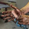 Two dirt-covered hands showing calluses and wear from manual labor in a workshop setting