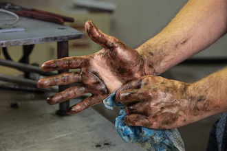 Two dirt-covered hands showing calluses and wear from manual labor in a workshop setting