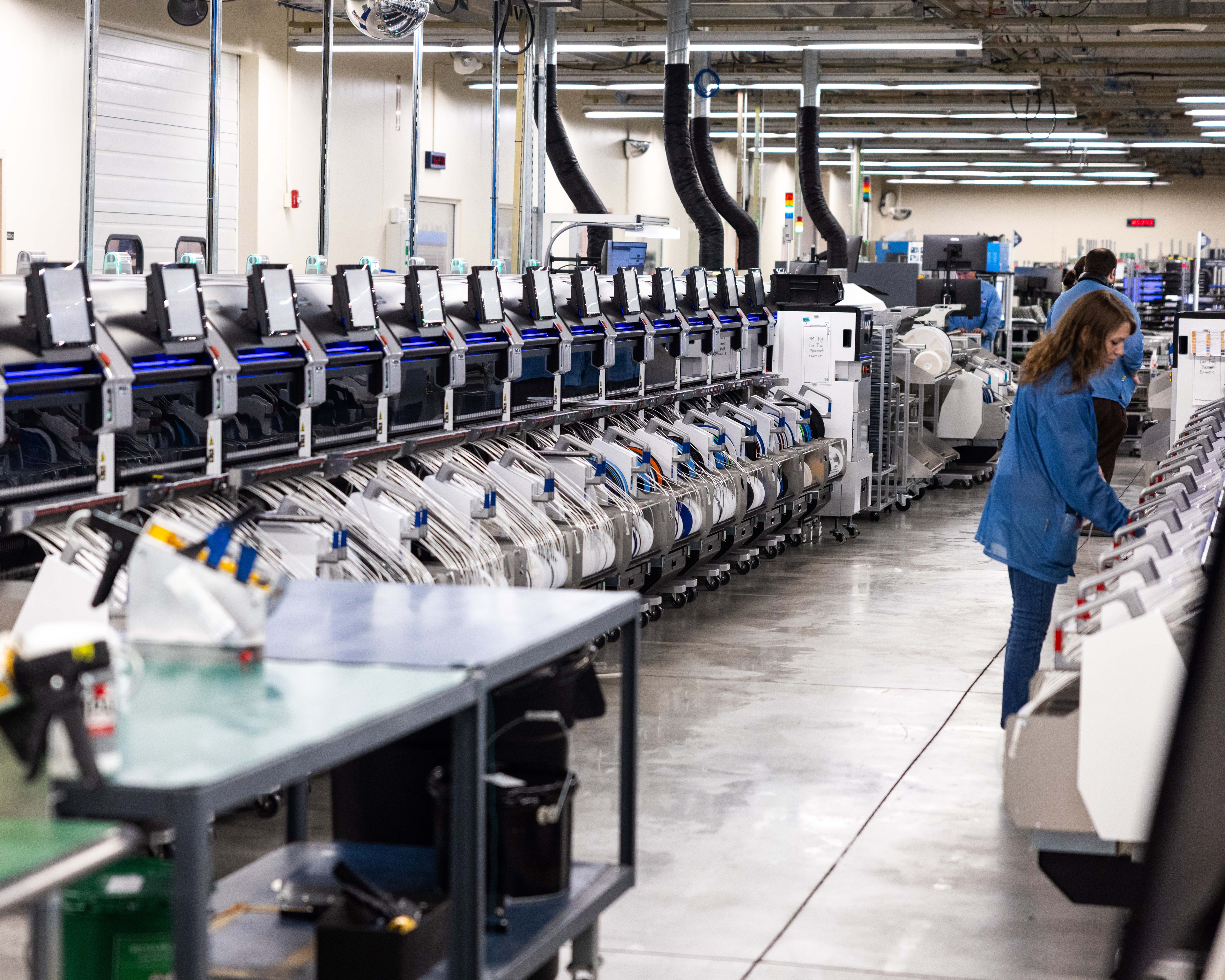 Industrial warehouse facility with rows of automated sorting machines and a worker in blue uniform monitoring operations