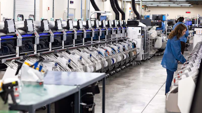 Industrial warehouse facility with rows of automated sorting machines and a worker in blue uniform monitoring operations