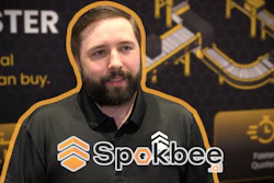 Man wearing Sparkbee branded black polo shirt at promotional event with gold and black backdrop