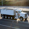 White Peterbilt dump truck traveling on a multi-lane highway with grassy hillside in background